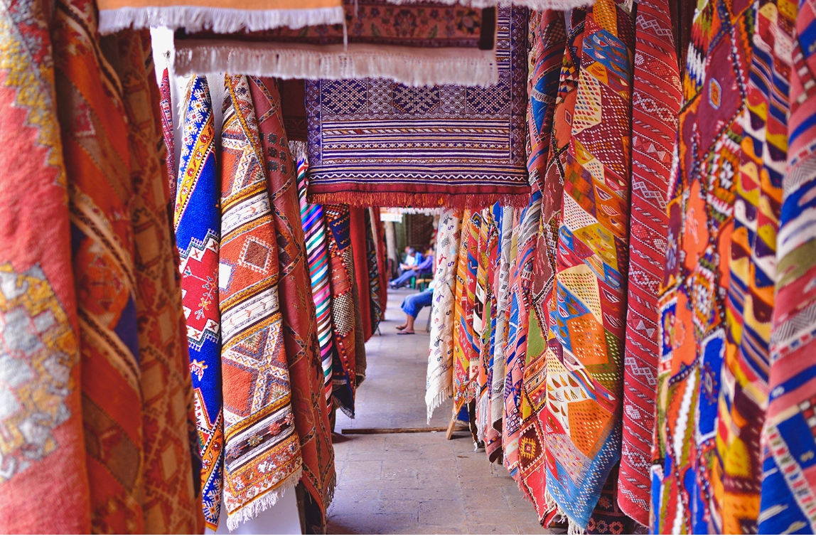 Colorful handwoven Moroccan rugs and textiles at a local market supported by Travel for Better